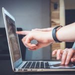two pairs of hands and a laptop. one hand points at the screen, the other appears to be scrolling on the trackpad.