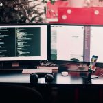 multi-screen workplace showing lines of code and headphones on the desk