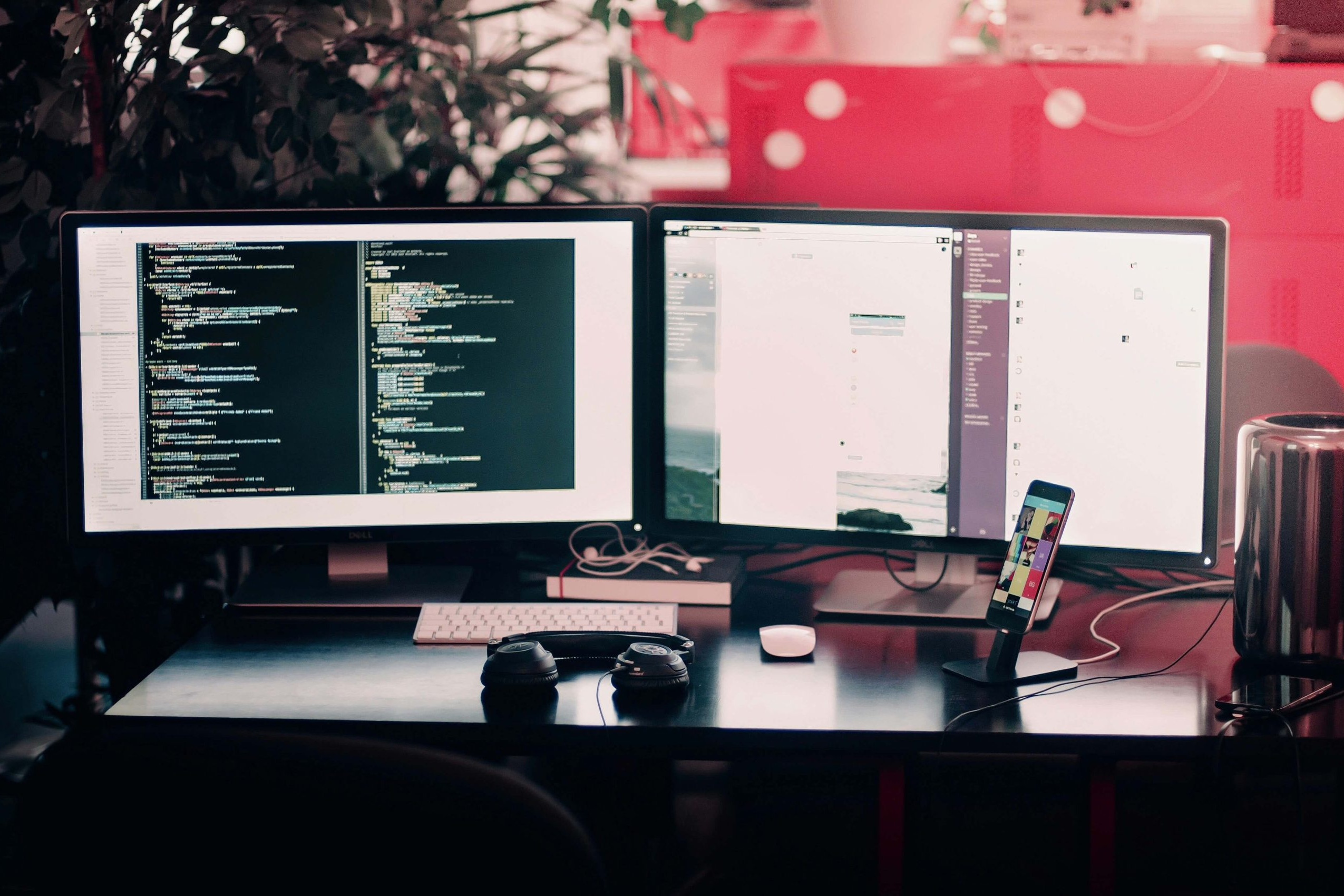 multi-screen workplace showing lines of code and headphones on the desk